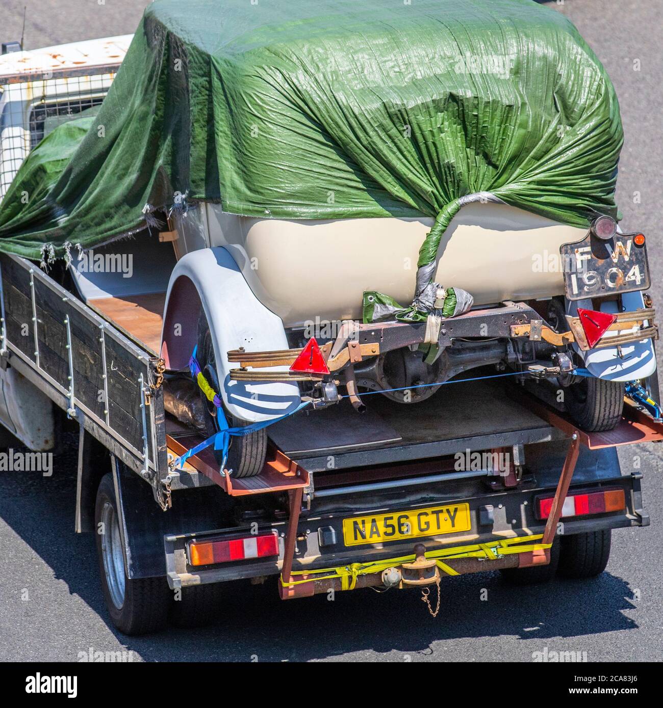 1931 1939cc Morris Major Motors restoration project rare barn find, vehicle restoration project, restore old wreck, classic car on Ford Transit 100 T350M RWD and wrapped in tarpaulin; UK Vehicular traffic, transport, pre-war saloon cars on lorry, automotive history on the M6 motorway highway. Stock Photo