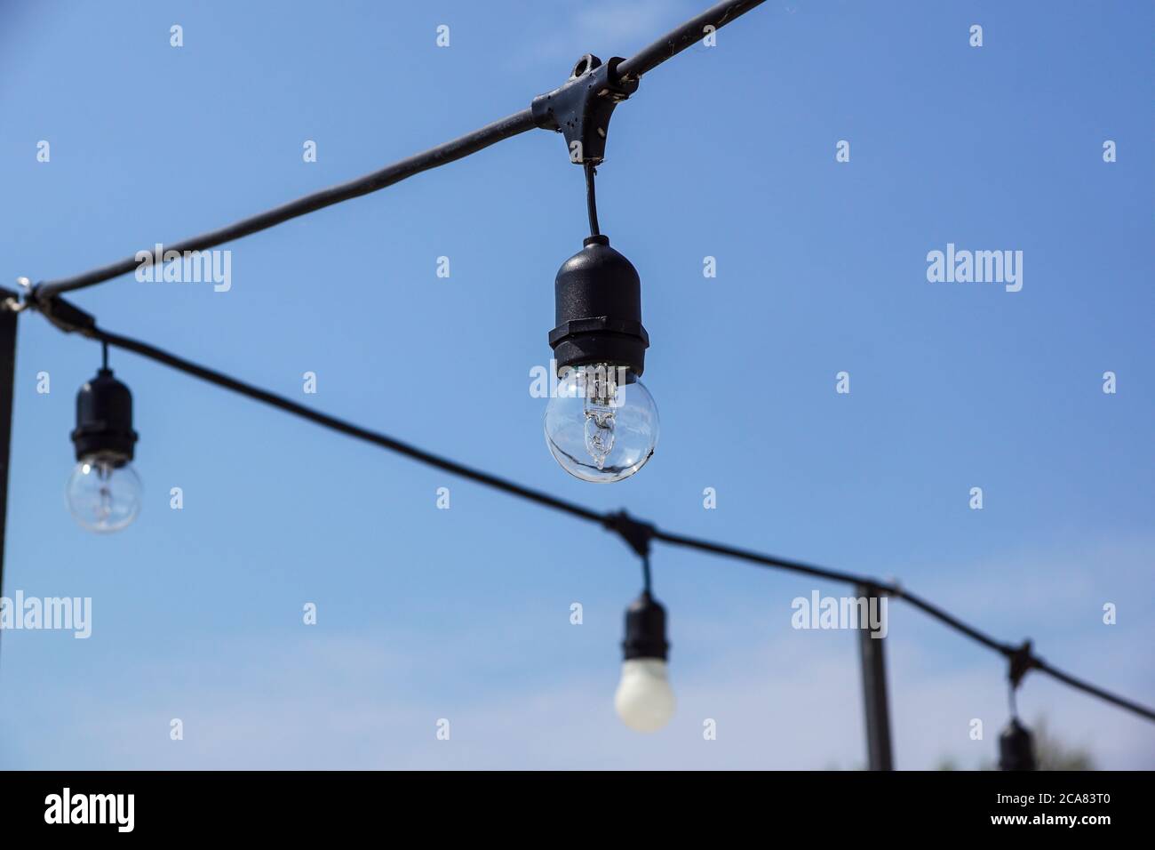 Close up of the glowing light bulbs at the beach cafe terrace. Sun is setting in the blurry abstract background Stock Photo