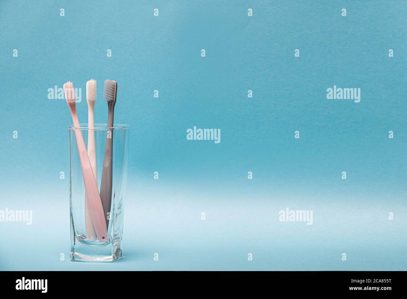 There is a toothbrush in a glass with a blue background. With copy