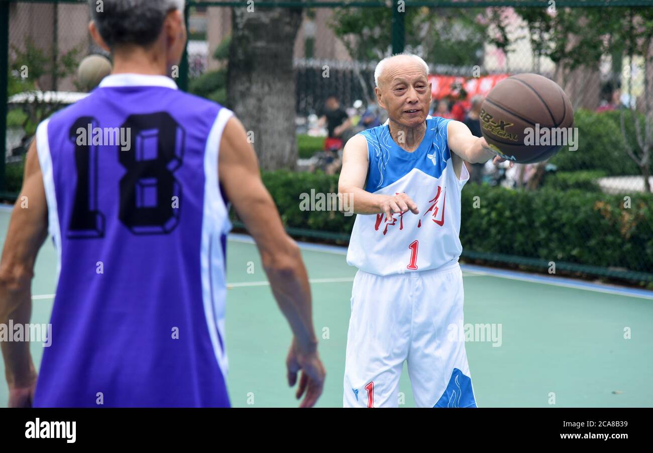 (200805) -- JINAN, Aug. 5, 2020 (Xinhua) -- Li Chunfu (R), 92, plays basketball with his teammate at an outdoor basketball court in Jinan, east China's Shandong Province, Aug. 5, 2020. As the oldest member of Jinan Senior Basketball Team which was founded in 2012, Li Chunfu has been playing basketball in his daily routine since 1949. Now in his 90s, Li practises basketball skills such as dribbling, layuping and shooting for half an hour to fourty minutes on average a day. 'Fitness requires consistency and regularity. Playing basketball and weight training make me maintain a good physical and m Stock Photo