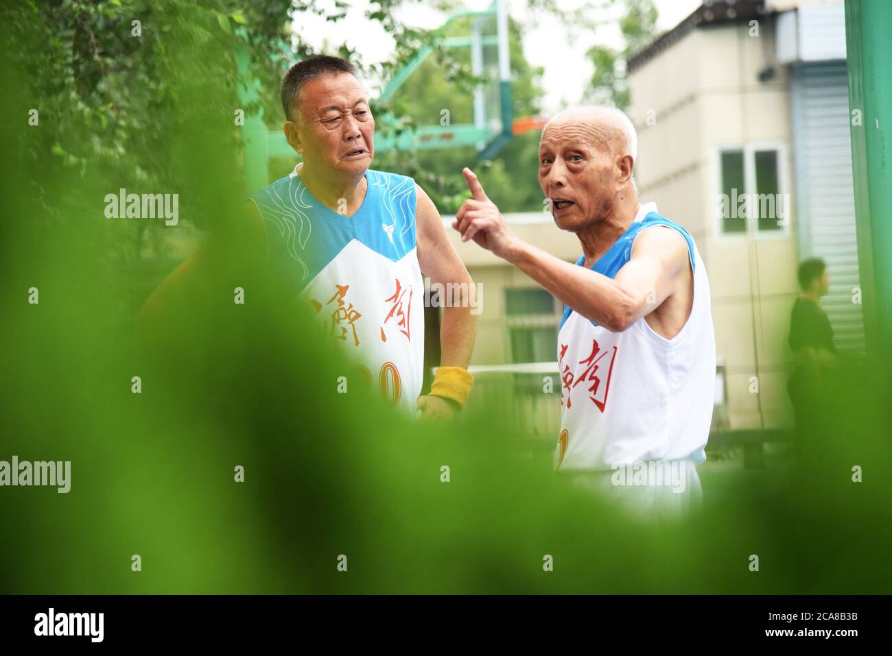 (200805) -- JINAN, Aug. 5, 2020 (Xinhua) -- Li Chunfu (C), 92, talks to his teammate during a training break at an outdoor basketball court in Jinan, east China's Shandong Province, Aug. 5, 2020. As the oldest member of Jinan Senior Basketball Team which was founded in 2012, Li Chunfu has been playing basketball in his daily routine since 1949. Now in his 90s, Li practises basketball skills such as dribbling, layuping and shooting for half an hour to fourty minutes on average a day. 'Fitness requires consistency and regularity. Playing basketball and weight training make me maintain a good phy Stock Photo