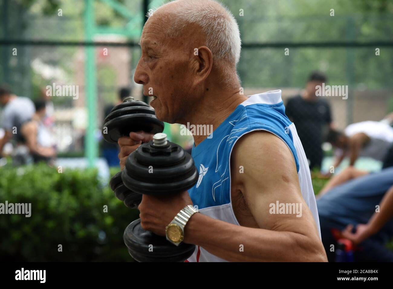 (200805) -- JINAN, Aug. 5, 2020 (Xinhua) -- Li Chunfu, 92, life dumbells before baksetball training at an outdoor basketball court in Jinan, east China's Shandong Province, Aug. 5, 2020. As the oldest member of Jinan Senior Basketball Team which was founded in 2012, Li Chunfu has been playing basketball in his daily routine since 1949. Now in his 90s, Li practises basketball skills such as dribbling, layuping and shooting for 30 to 40 minutes on average a day. 'Fitness requires consistency and regularity. Playing basketball and weight training make me maintain a good physical and mental state. Stock Photo