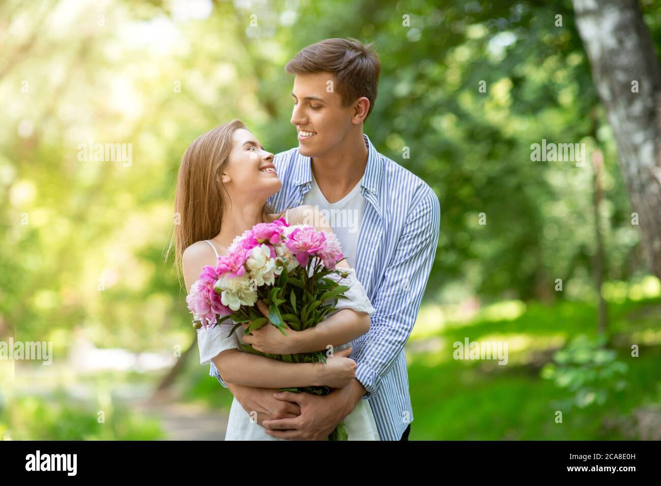 Celebrating anniversary. Young girl with flowers looking affectionately at boyfriend in park Stock Photo