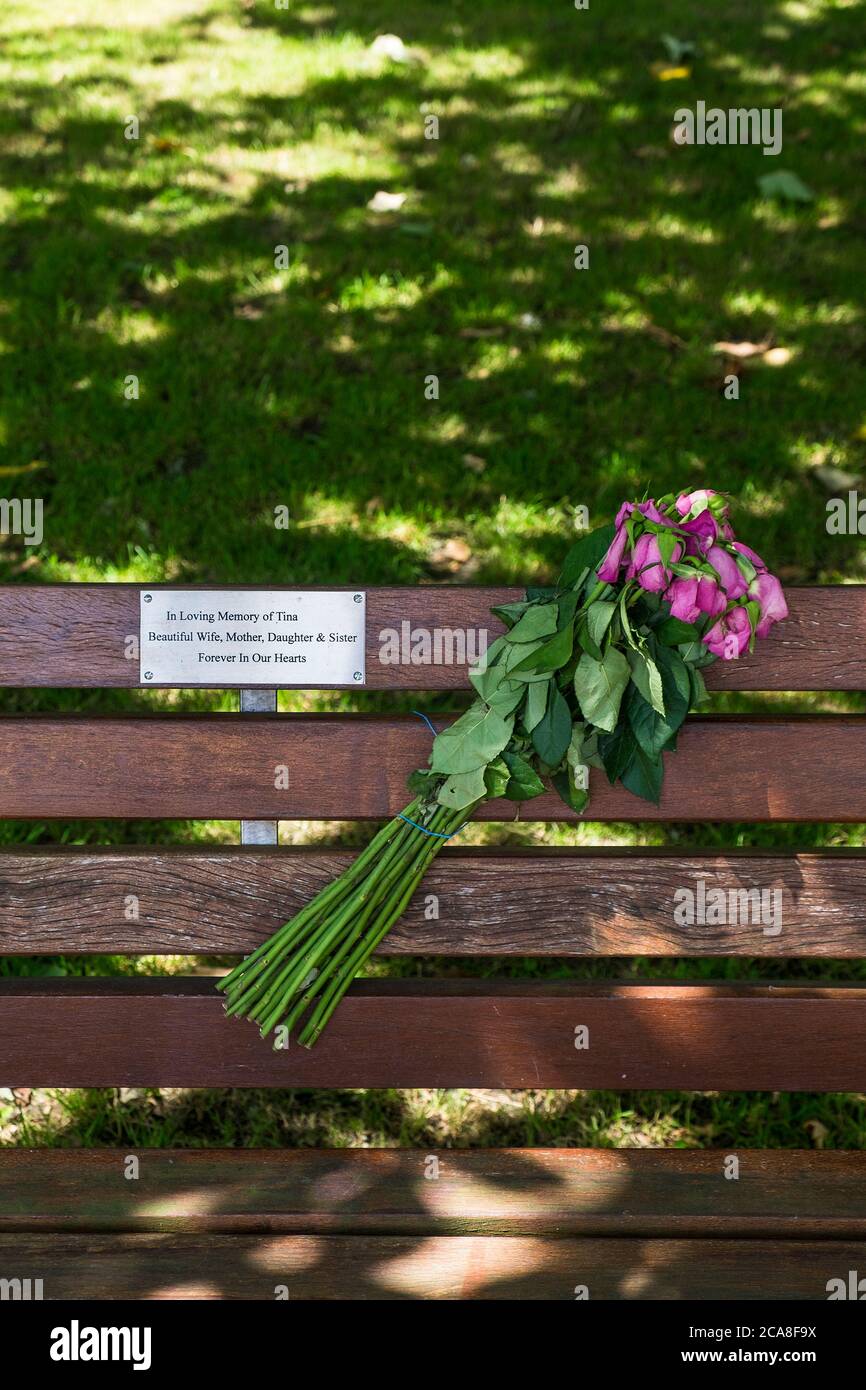 A bouquet of wilting flowers attached to a memorial bench in a park. Stock Photo