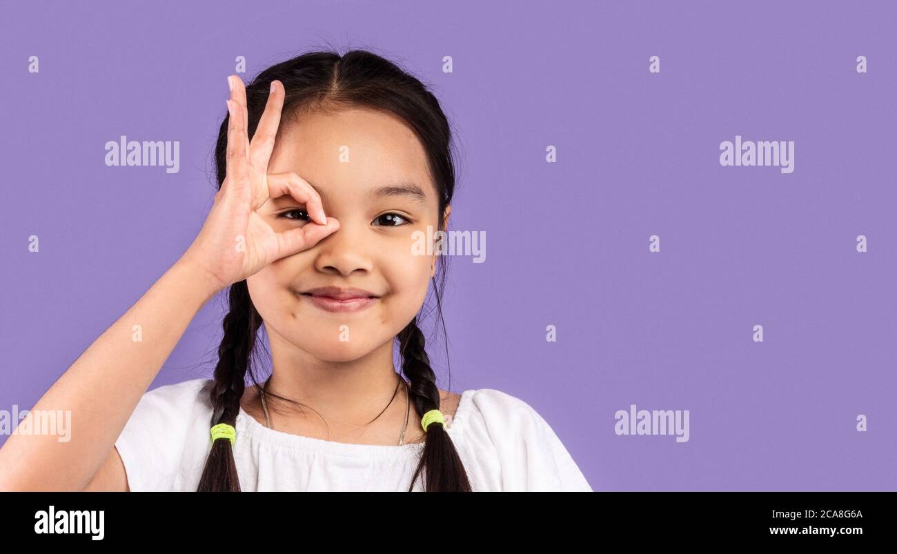 Asian Girl Covering Eye With OK Sign Posing In Studio Stock Photo