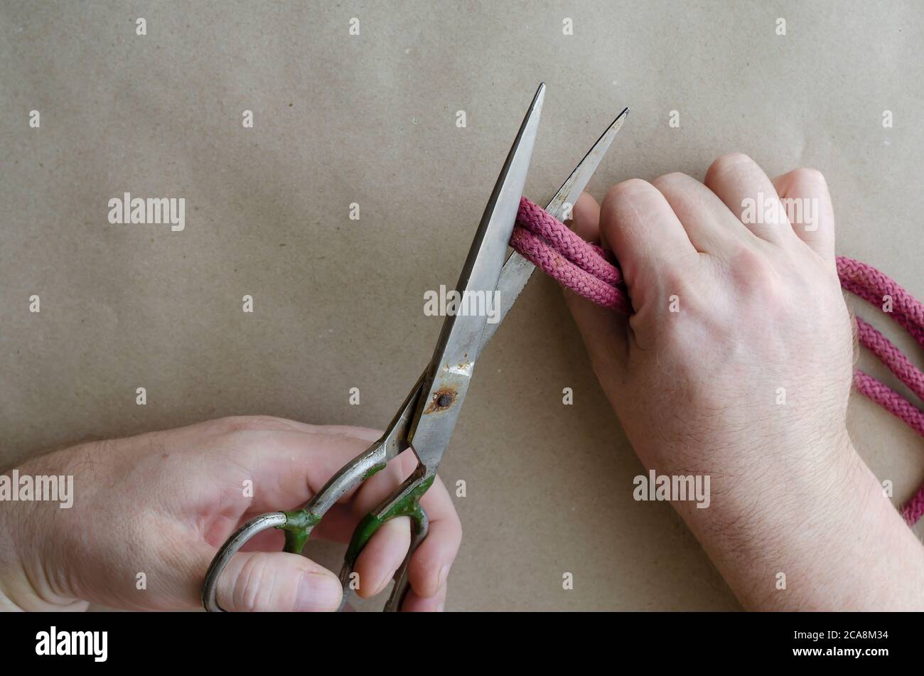 Hand Cutting Rop An adult Caucasian man's hand cuts the red rope with old metal scissors ...