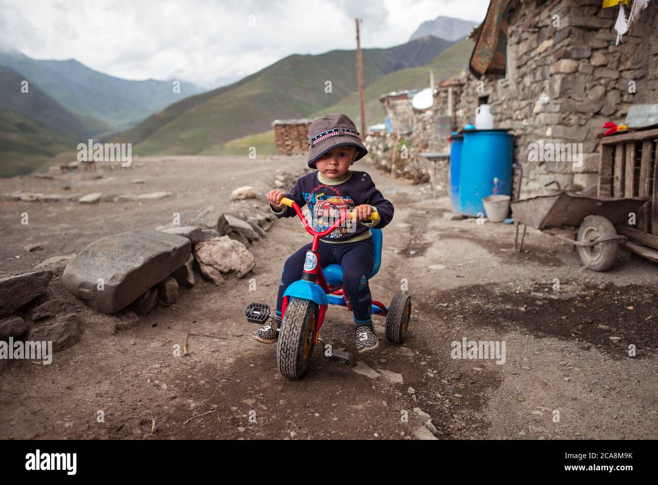 Xinaliq / Azerbaijan - July 8, 2019: Portrait of cute kid riding colorful small bicycle in mountain village Stock Photo