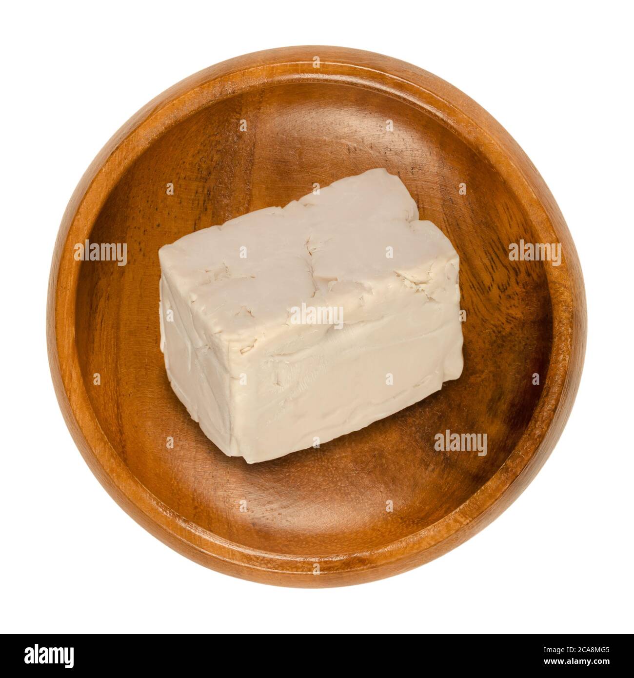 Fresh bakers yeast block in a wooden bowl. Compressed fresh yeast, used in baking as leavening agent to convert sugars in dough to carbon dioxide. Stock Photo