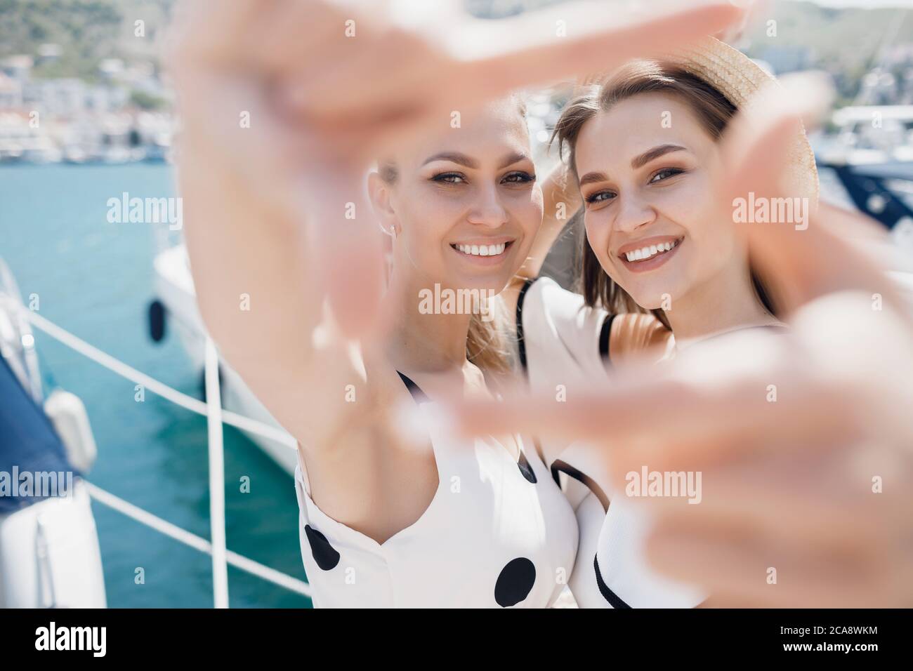 Portrait of a two beautiful young smiling woman doing selife with frame ...