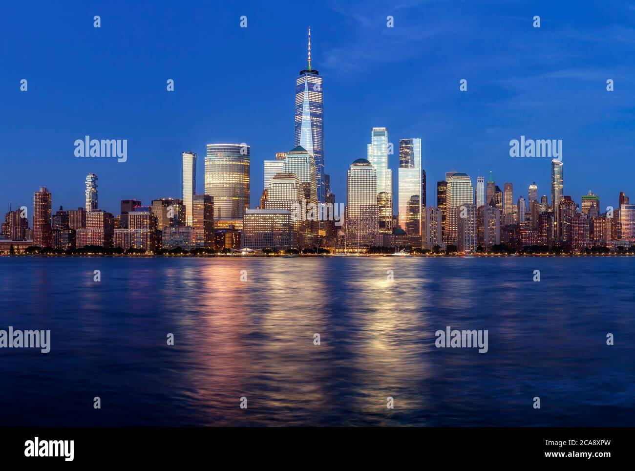 Manhattan skyline at dusk with city lights reflected in water, New York ...