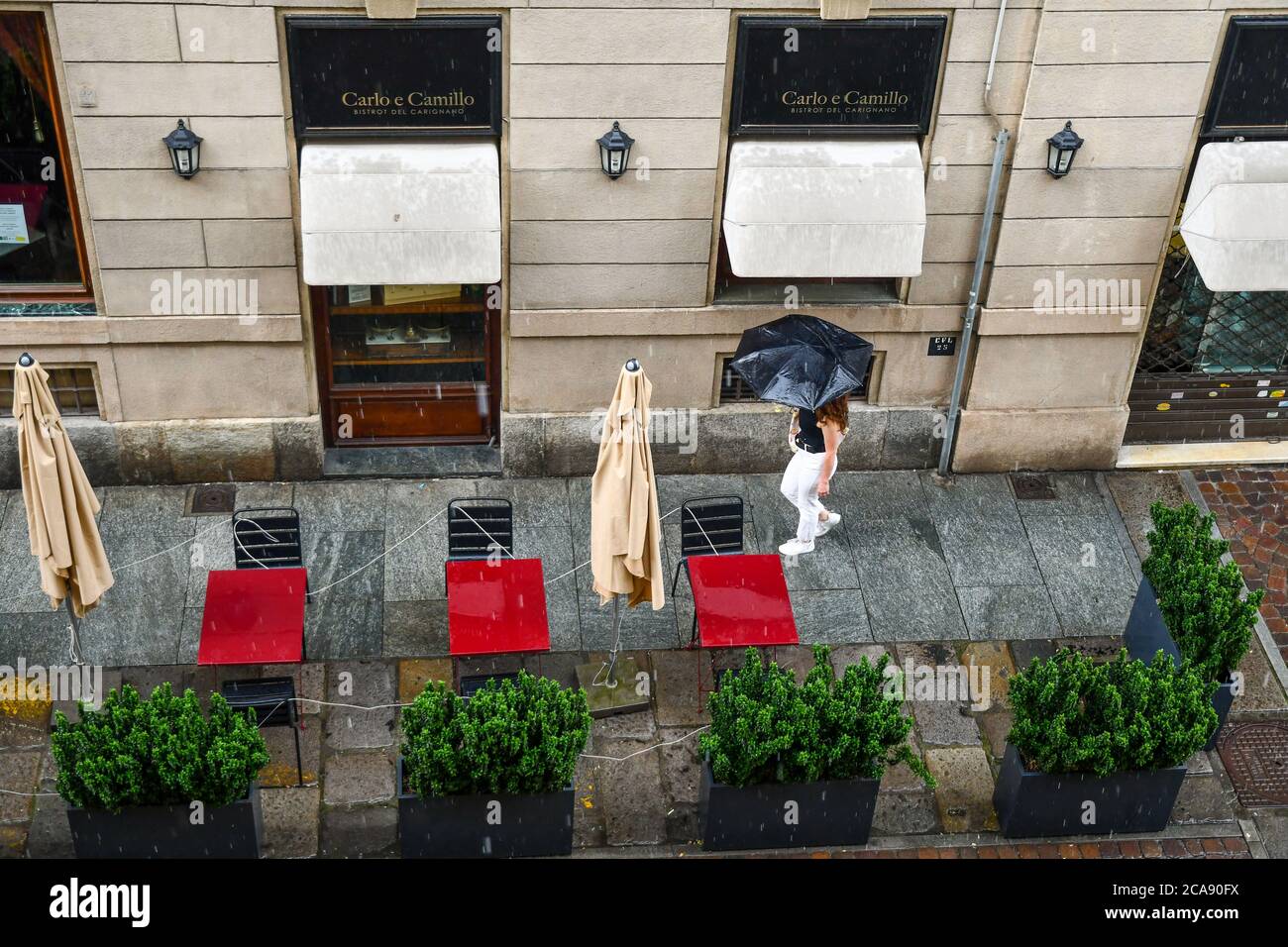 High angle view of a girl walking with an umbrella on the sidewalk of a closed pavement restaurant in a rainy day, Turin, Piedmont, Italy Stock Photo