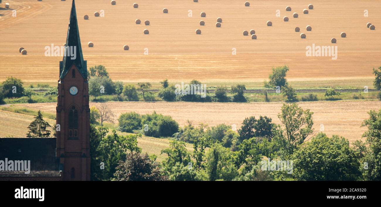 Rinteln, Germany. 05th Aug, 2020. Straw rolls lie on a field in sight of the St.Agnes church Steinbergen in the district of Schaumburg. Credit: Julian Stratenschulte/dpa/Alamy Live News Stock Photo