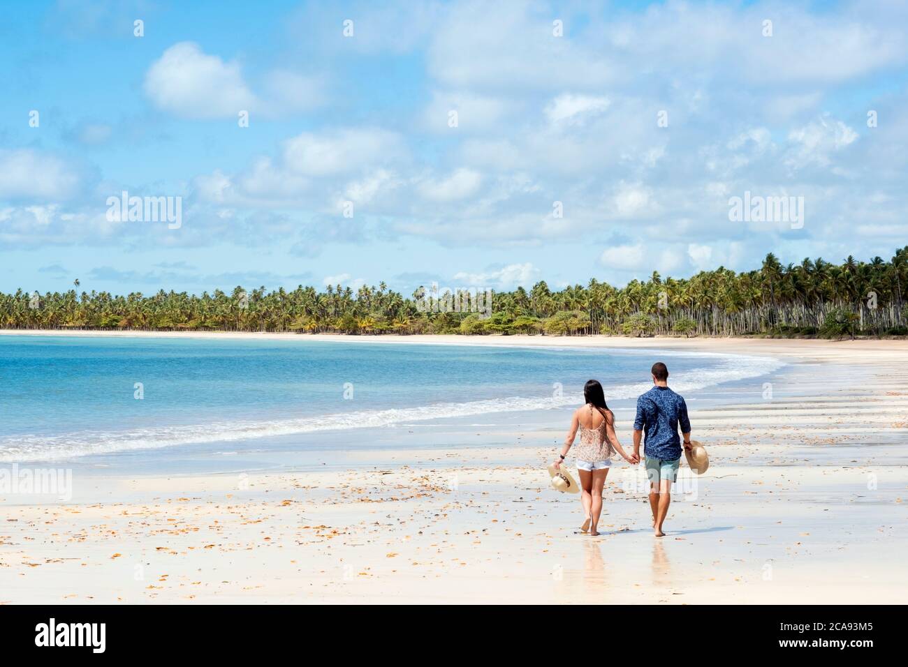 A good-looking Hispanic (Latin) couple walking on a deserted beach with backs to camera, Brazil, South America Stock Photo