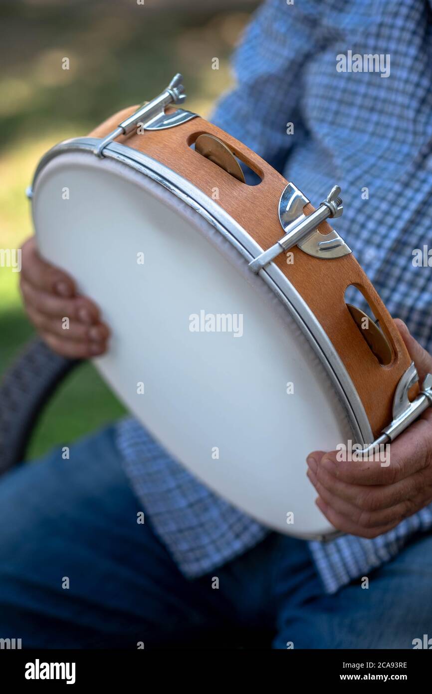 Man holds in his hand a folk tambourine in greece. Side profile of a man playing a tambourine Instrument. Stock Photo
