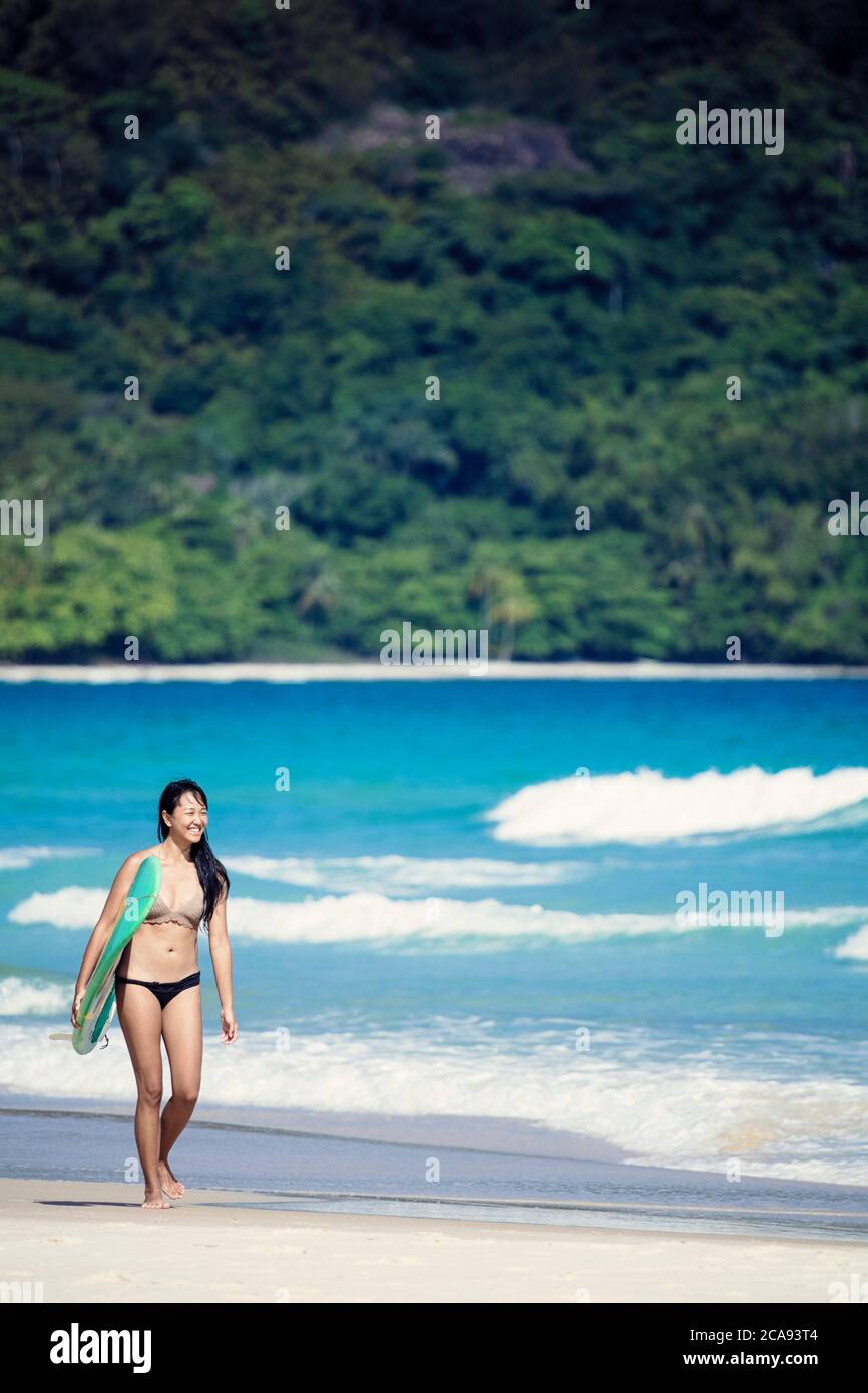 Beach shot of a Japanese Brazilian (Nipo-brasileiro) in a bikini carrying a surf board decorated with the Brazilian flag, Brazil, South America Stock Photo