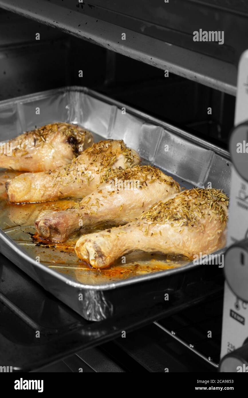 Chicken drumsticks with rosemary cooking in a foil tray in an oven