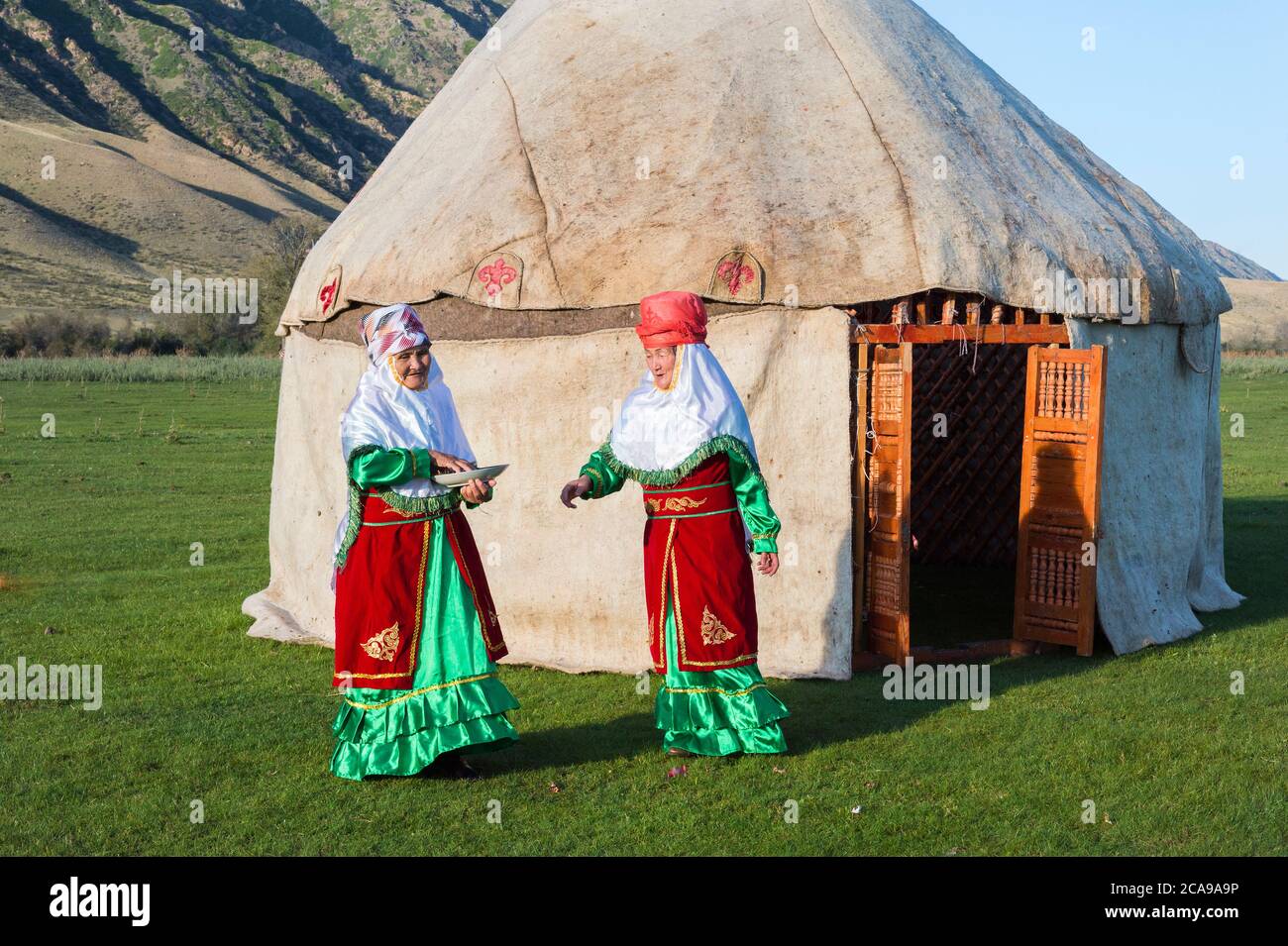 Two Kazakh women in traditional clothes in front of a yurt welcoming guests with candies, For editorial Use only, Sati village, Kazakhstan Stock Photo