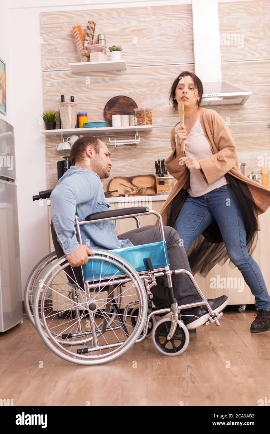 Disabled man in wheelchair singing with his wife in kitchen. Young