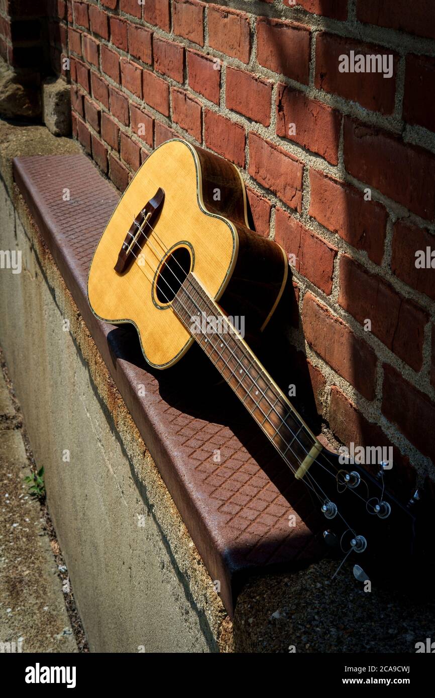 Acoustic baritone ukulele guitar left outside performance venue againts