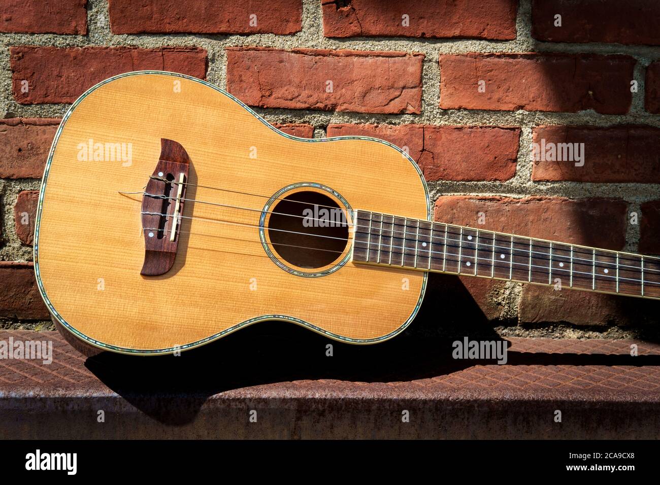 Acoustic baritone ukulele guitar left outside performance venue againts