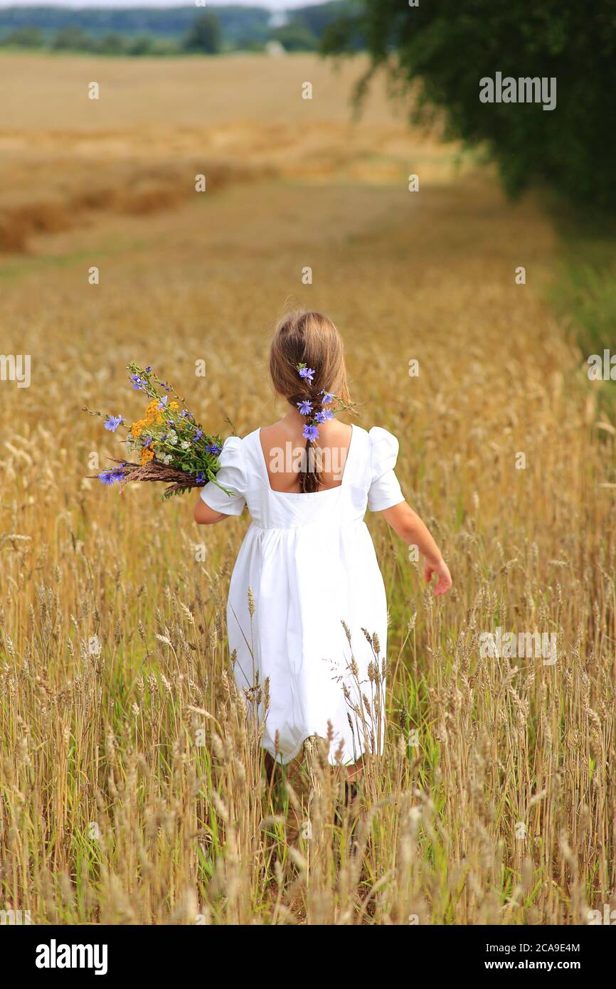 Little girl with a bouquet of wildflowers in her hands in a wheat field ...