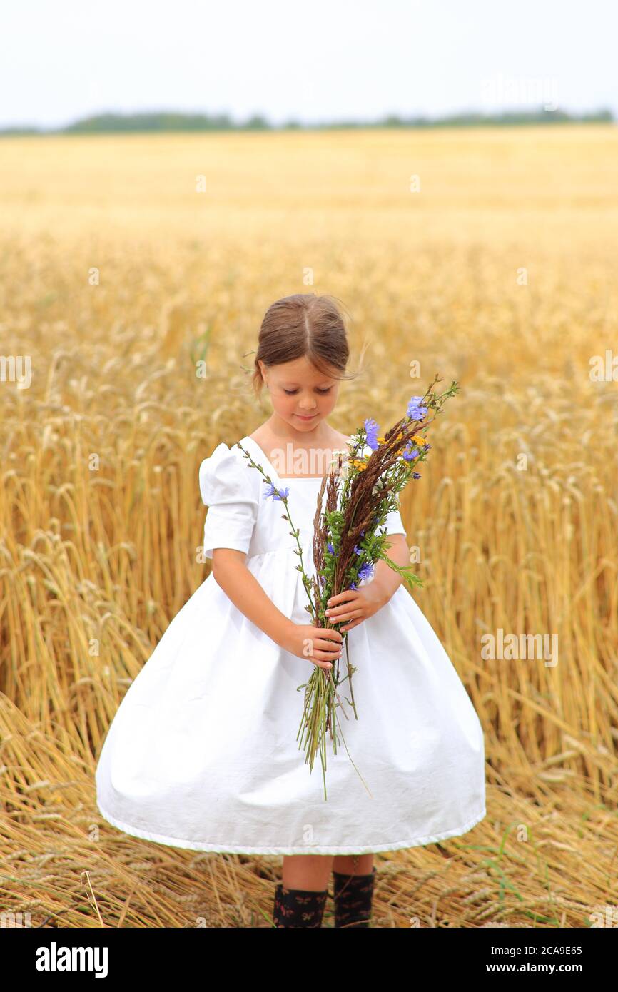 Little girl with a bouquet of wildflowers in her hands in a wheat field ...