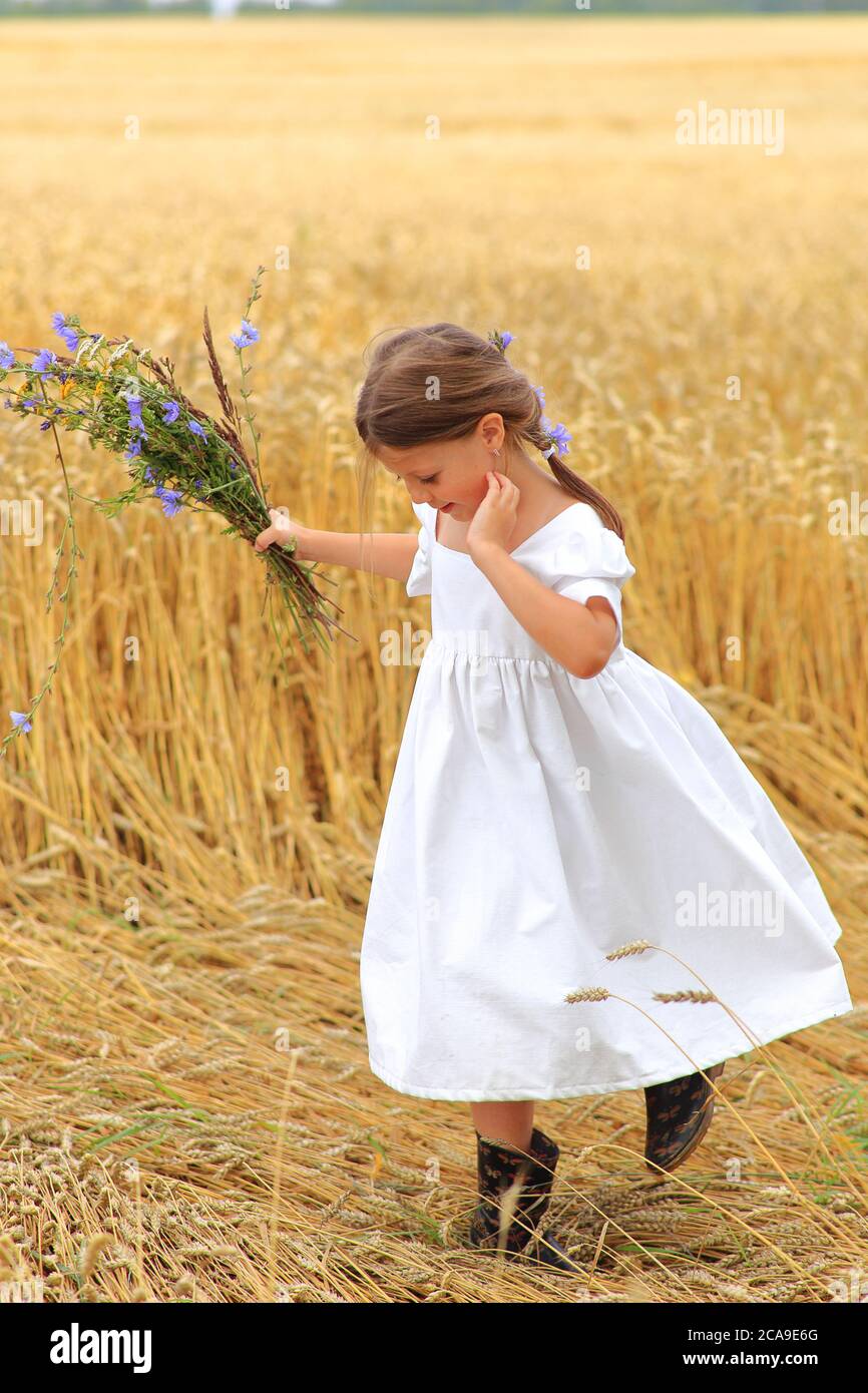 Little girl with a bouquet of wildflowers in her hands in a wheat field ...