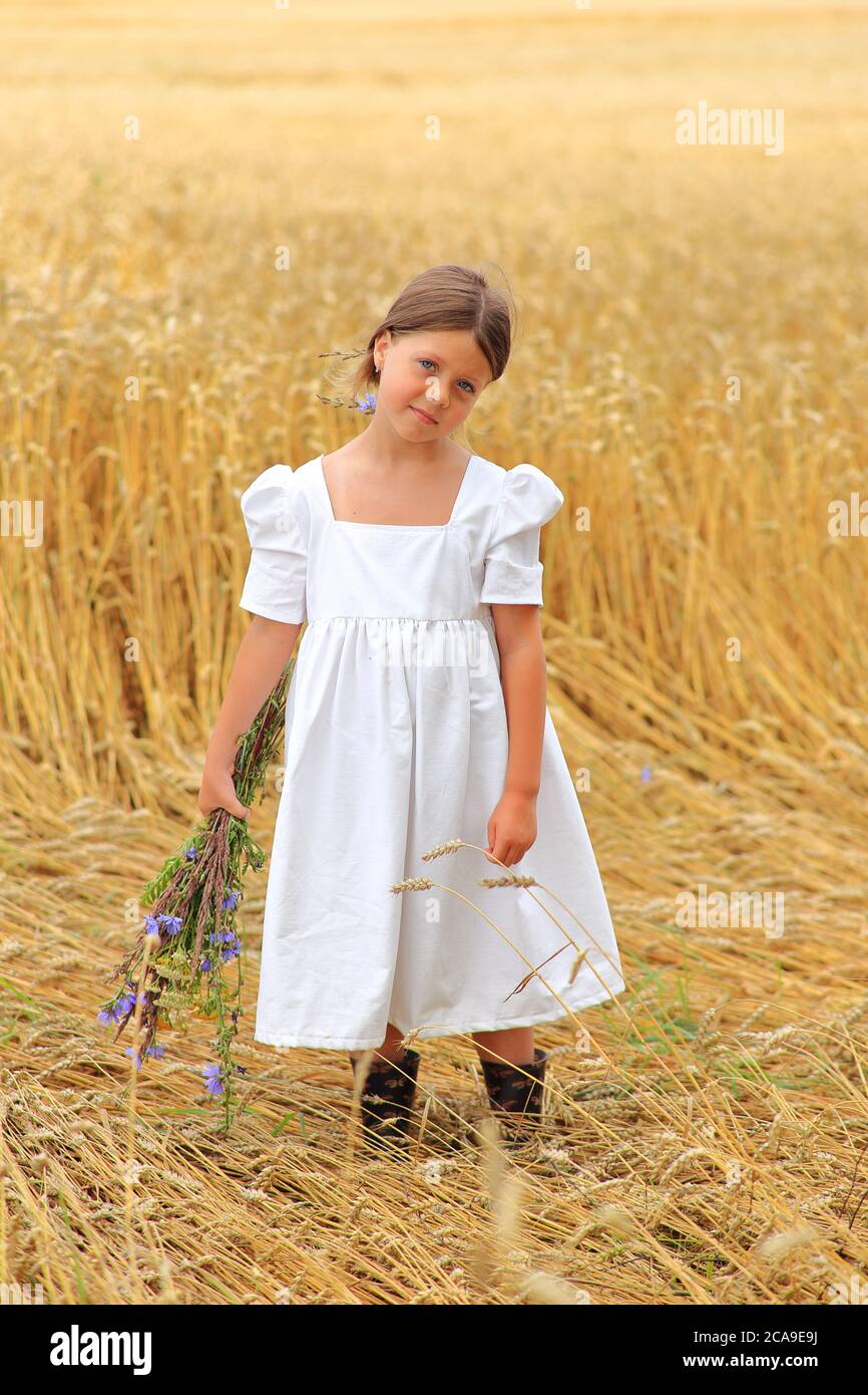 Little girl with a bouquet of wildflowers in her hands in a wheat field ...