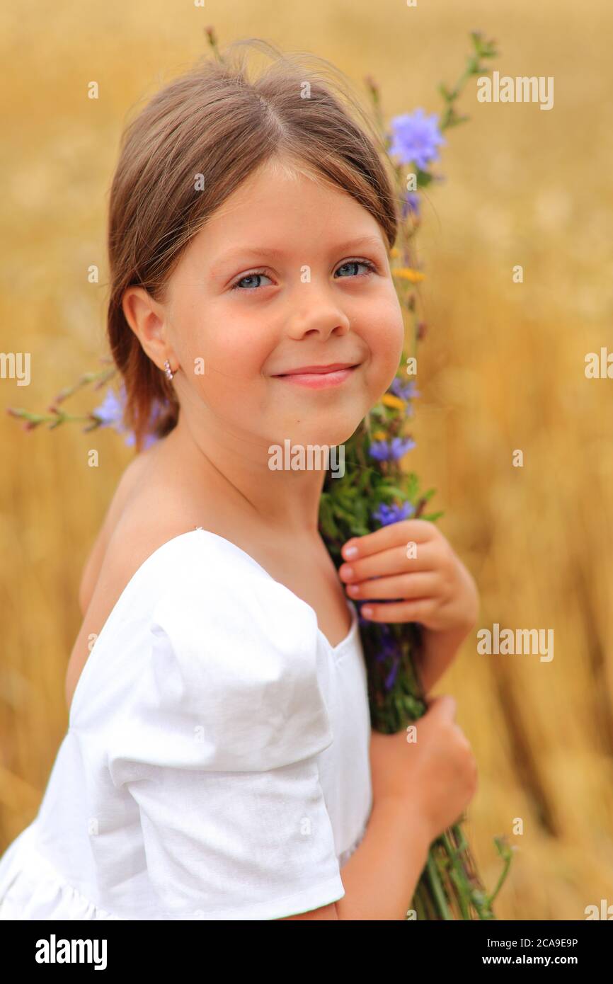 Little girl with a bouquet of wildflowers in her hands in a wheat field ...