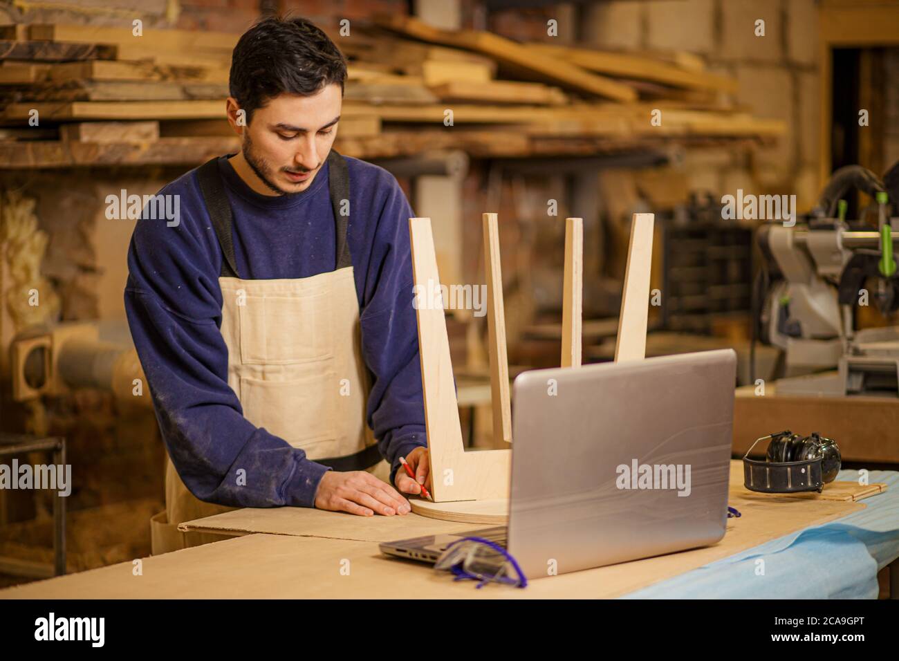 young furniture maker skillfully make a wooden chair on a workbench and use laptop while working