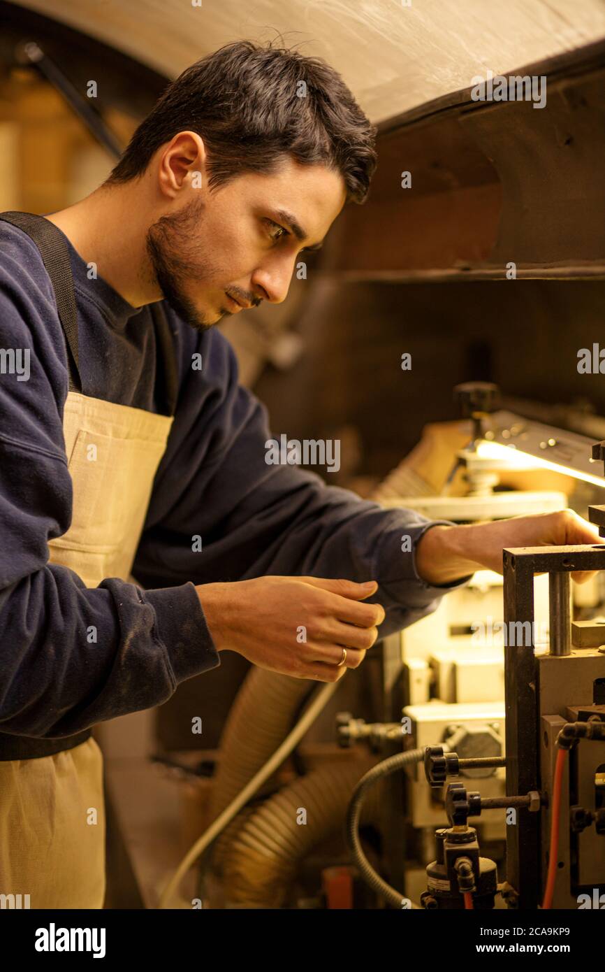 portrait of concentrated carpenter man at work place, skillful guy in uniform make furniture on an order for cutomers Stock Photo