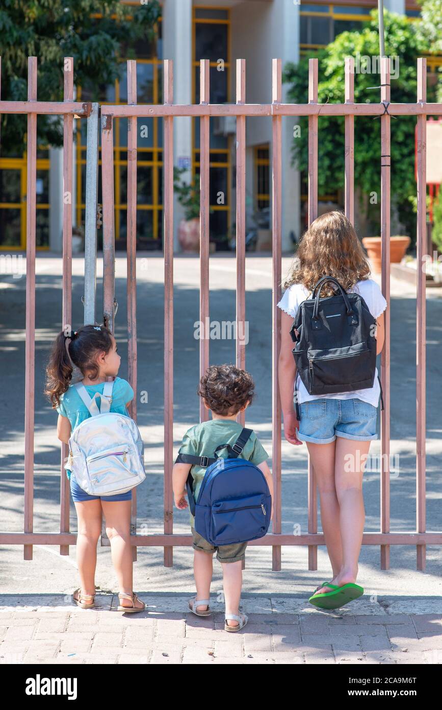 A Young Sisters And Brother Wait Outisde A Closed School Gate. Diverse