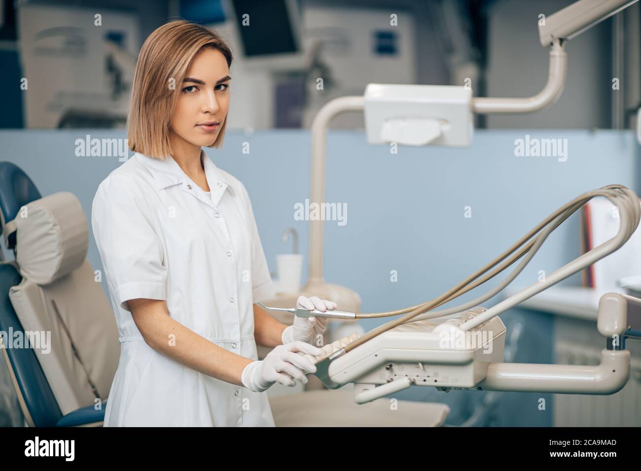 serious young dentist woman at work, use special instrument equipment for teeth treatment, look at camera, health care provider Stock Photo