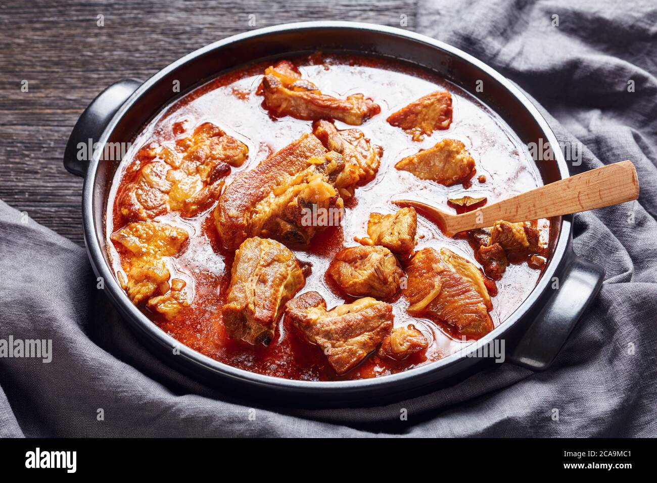 braised pork brisket chunks in a black dutch oven on a dark wooden table, landscape view from above, close-up Stock Photo