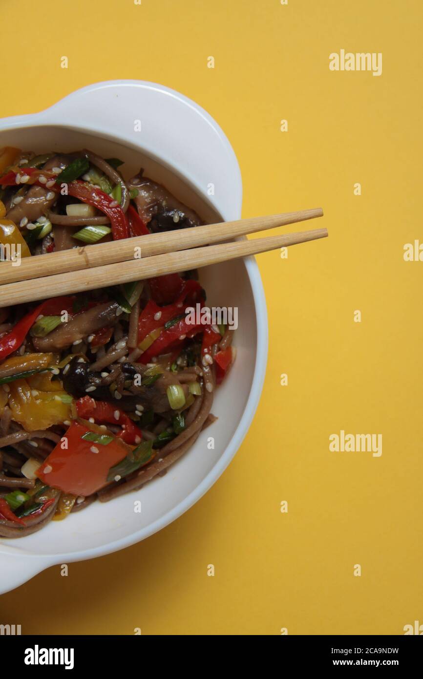 a bowl of wok noodles and chopsticks isolated on yellow background flat lay extreme close up. Image contains copy space Stock Photo