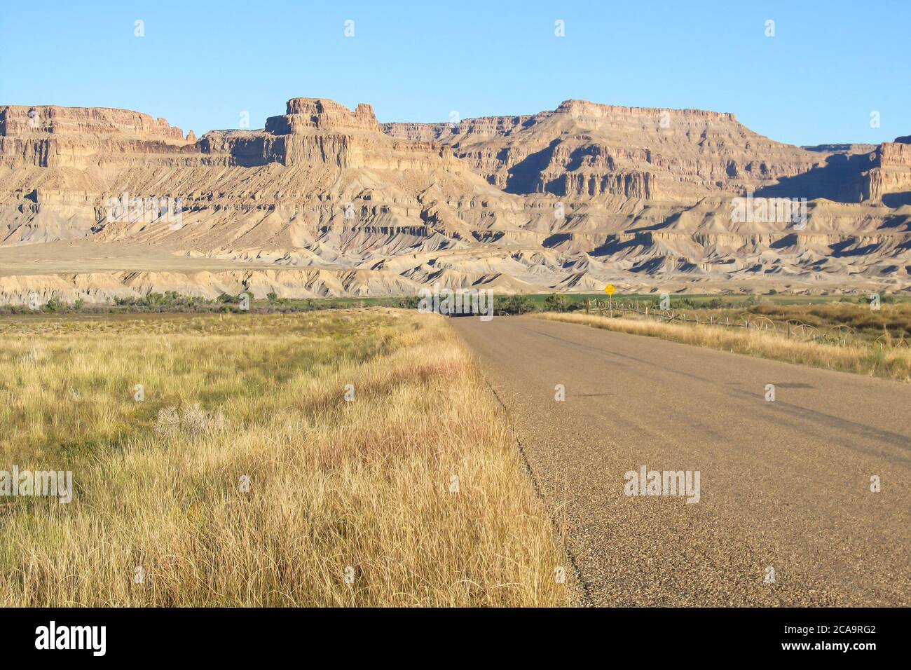 A Tar road cutting through the grasslands of Eastern Utah, USA, with the Bookcliffs rising in the background Stock Photo
