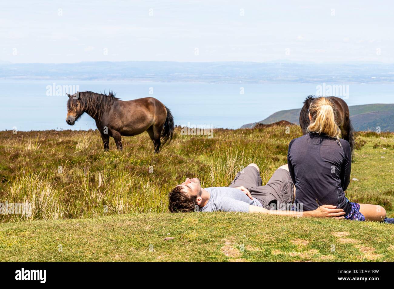 Exmoor National Park - A young couple and ponies relaxing on the highest point of Exmoor, Dunkery Beacon 1705 feet 520 metres, Somerset UK Stock Photo