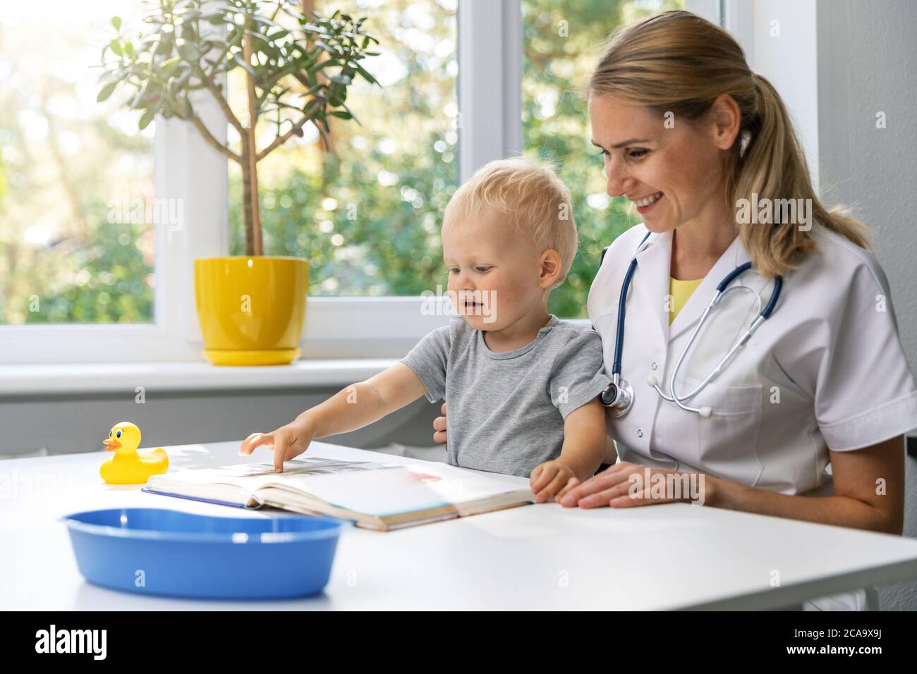 pleasant doctor and child watching book together at desk in clinic office. little boy at pediatrician visit Stock Photo