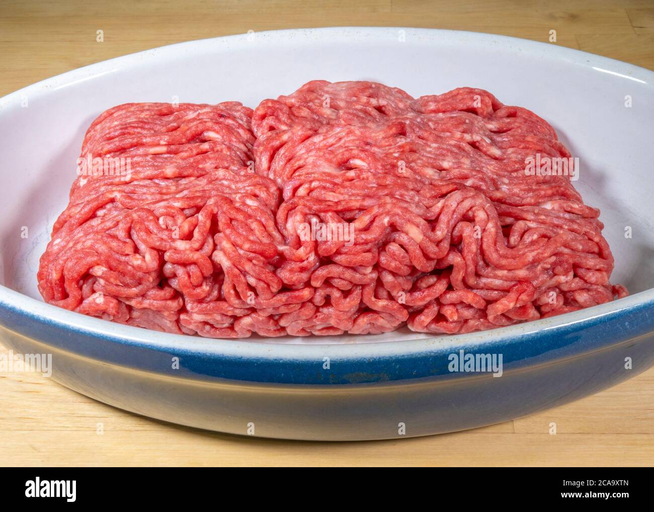 Raw supermarket British beef steak mince in a ceramic bowl, after defrosting from frozen, ready to be cooked. 500 grammes in weight.10% fat content. Stock Photo
