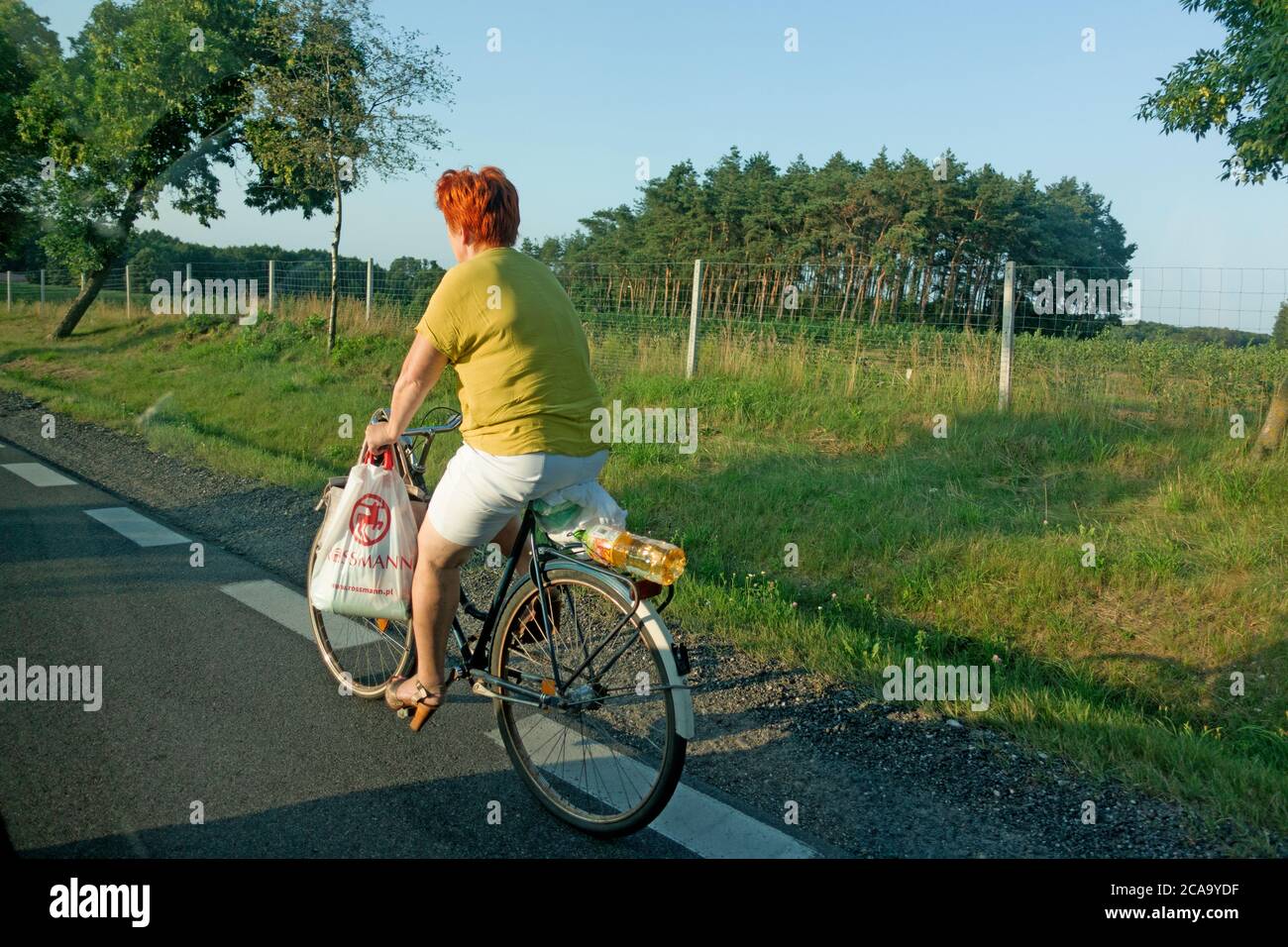 Attractive Polish woman with red hair wearing heals riding a bicycle carrying groceries home. Zawady Gmina Rzeczyca Poland Stock Photo