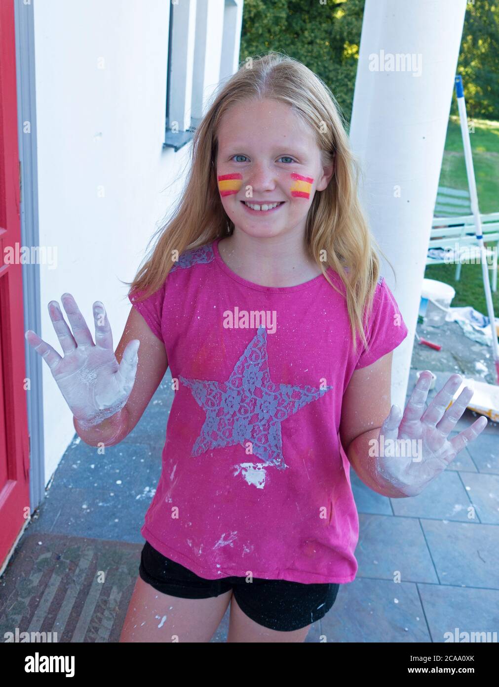 Polish preteen girl showing painted hands from painting house and yellow red stripes on cheeks with a star on her shirt. Zawady Gmina Rzeczyca Poland Stock Photo