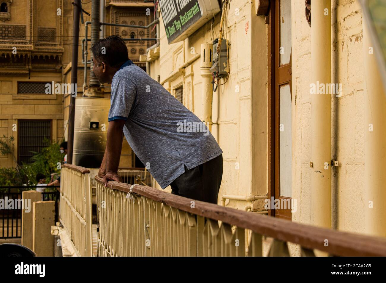 jaisalmer, rajasthan / india - CIRCA july 2020 : middle aged man enjoys watching outside of his house, leans on the balcony railing during corona viru Stock Photo