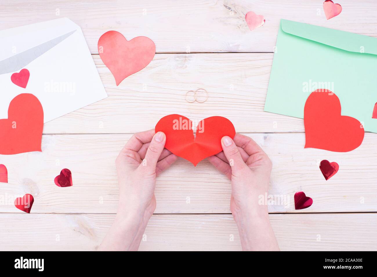 Female hands hold a broken heart with wedding rings on a wooden table. Marriage problems, divorce Stock Photo