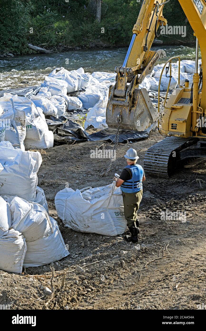 A flood mitigation construction crew using an excavator to lift heavy bags of rocks to stabilize the river banks of the Elbow River, Calgary Canada Stock Photo