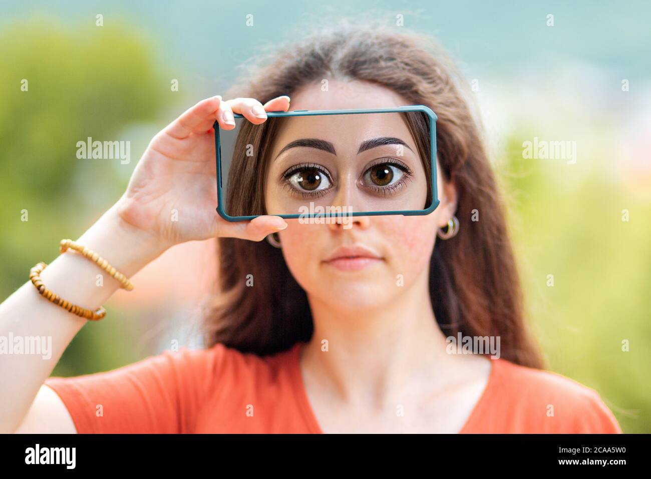 A woman closes her eyes with a smartphone, with a picture of huge cartoon eyes. The concept of hiding identity and fake pages in social networks. Stock Photo