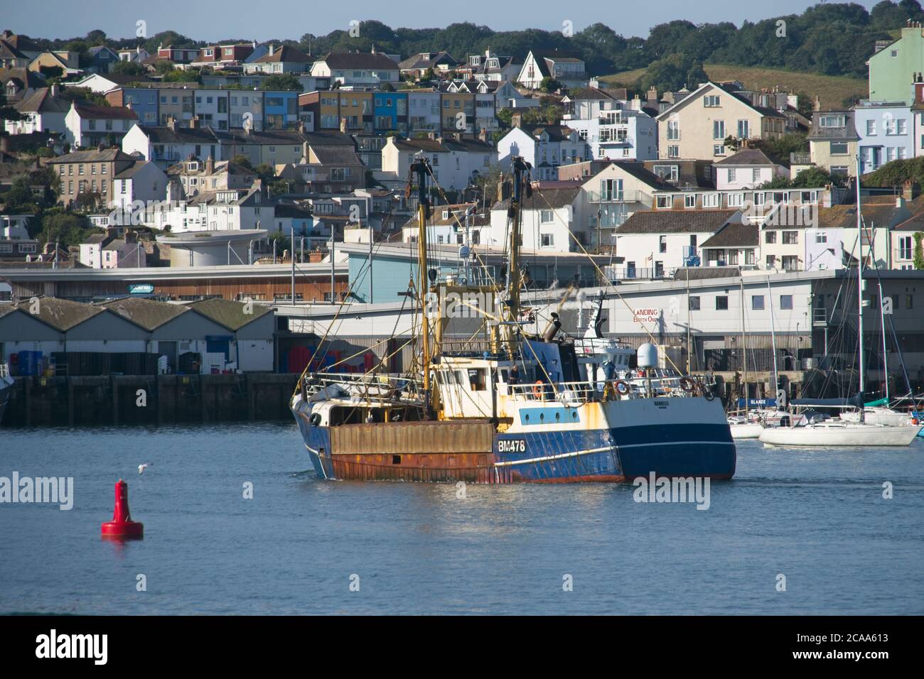 Brixham Trawler BM478 Danielle returning to port Commercial trawlers maneuvering in Brixham harbour Calm sea light blue sky Tiered Buildings behind Stock Photo