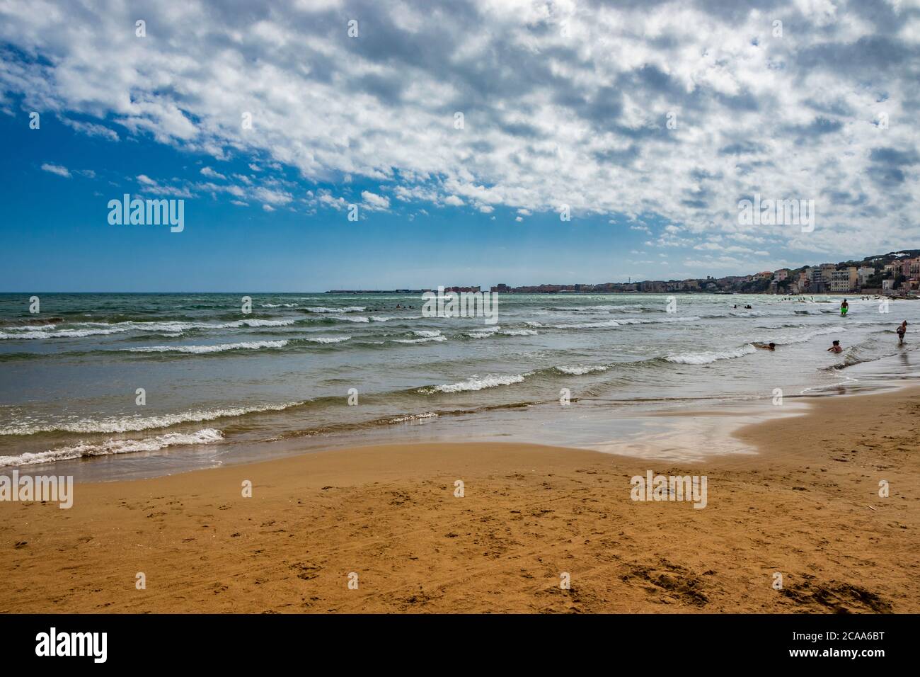 Nettuno, Lazio, Rome, Italy - Some people bathe, play and relax in the water, in the Roman sea. Reflections of light on the water. Cloudy blue sky at Stock Photo