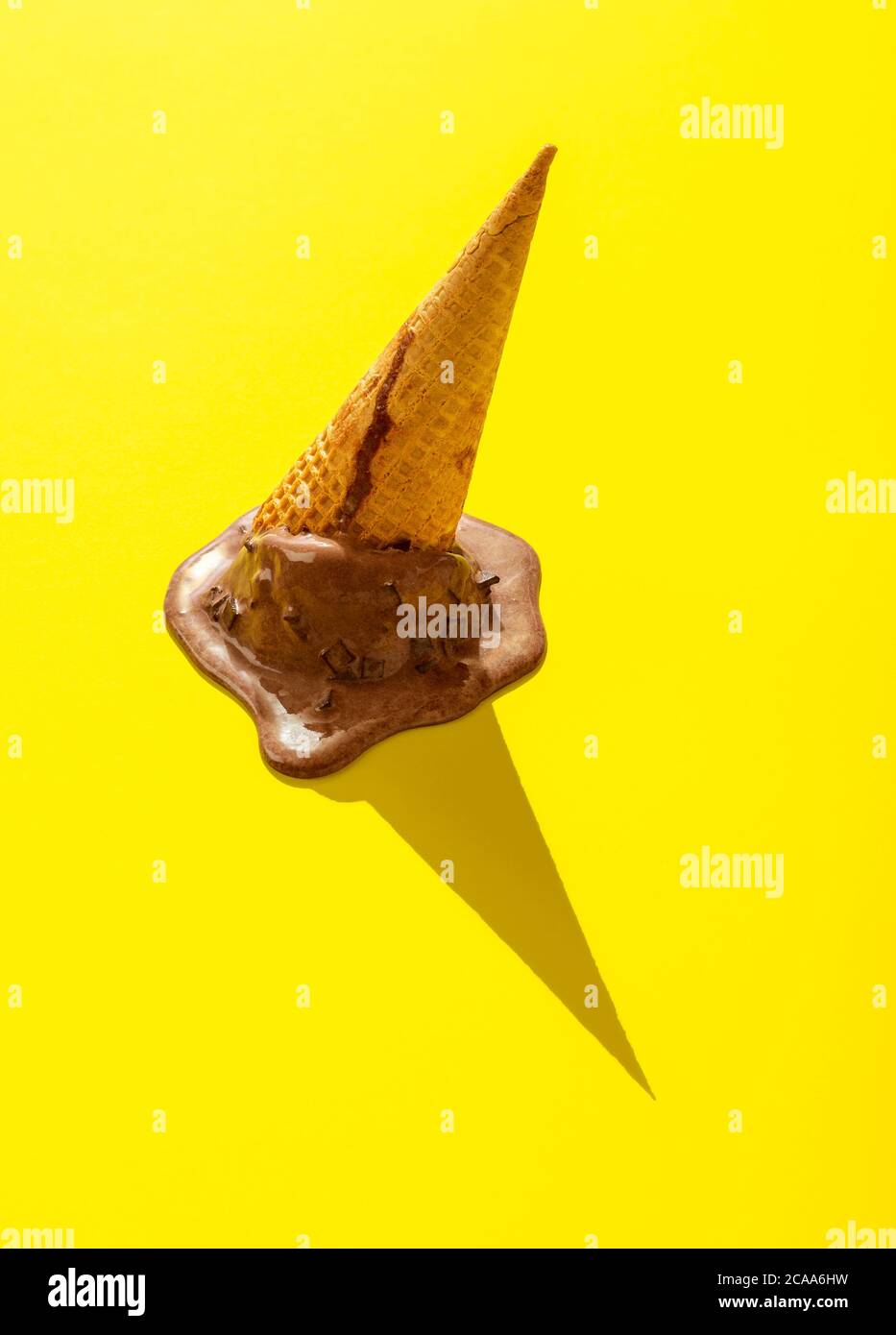 Upside down chocolate ice cream on a yellow background. Melting ice cream in bright light. Waffle cone ice cream isolated on a yellow-colored backgrou Stock Photo
