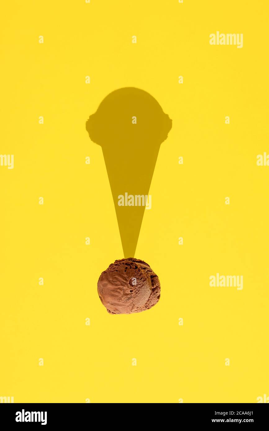 Creative layout of ice cream scoop with chocolate flavor, isolated on yellow background, with cone shadow. Funny concept for chocolate ice cream cone. Stock Photo