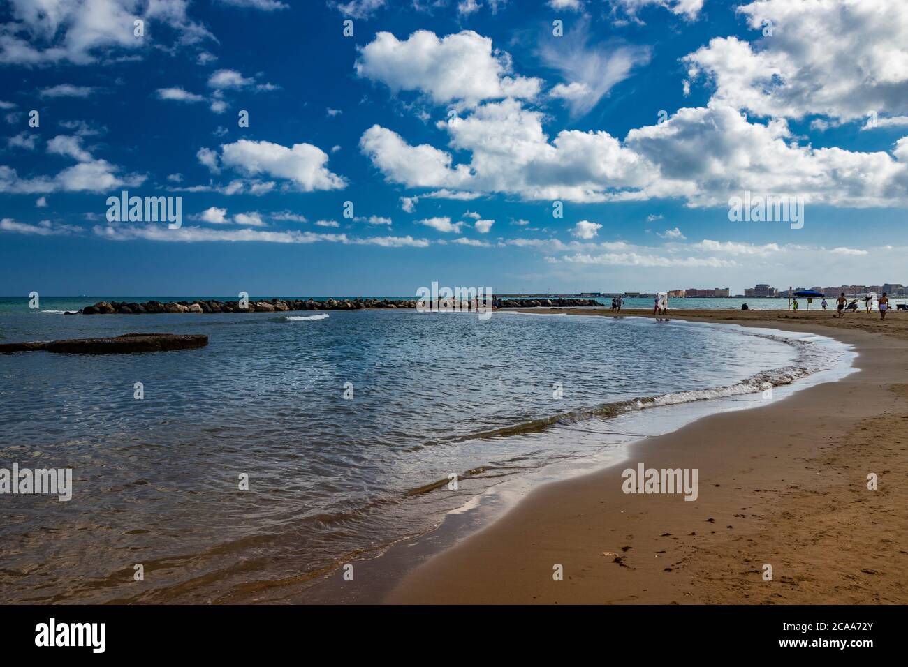 Nettuno, Lazio, Rome, Italy. Some people walk, play and relax on the shore, on the beach of the Roman sea. Backlit. Reflections of light on the water. Stock Photo
